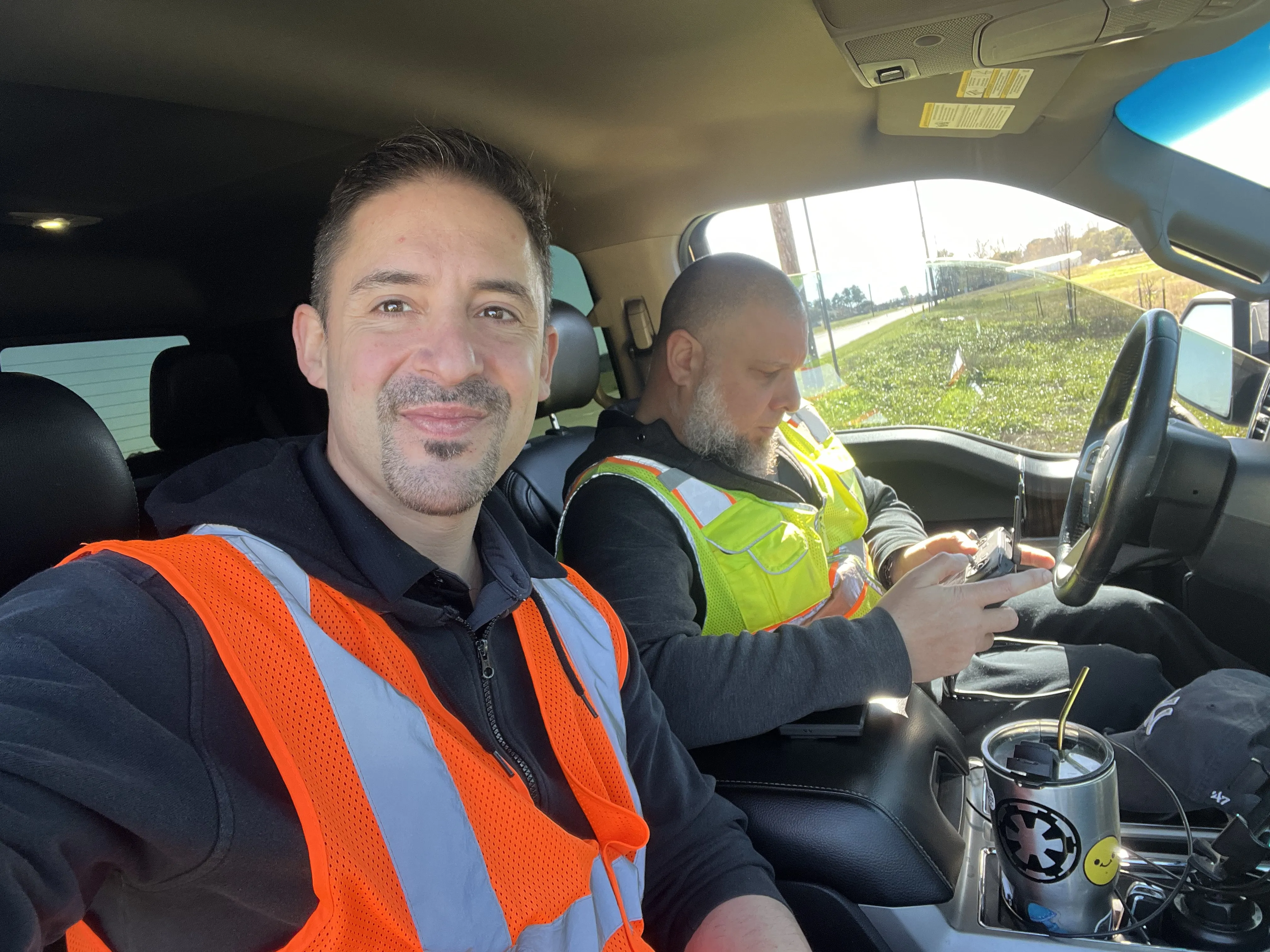 Two Axis crew members in high-visibility vests in the truck cab on a field site, one reviewing data on a handheld between flights.