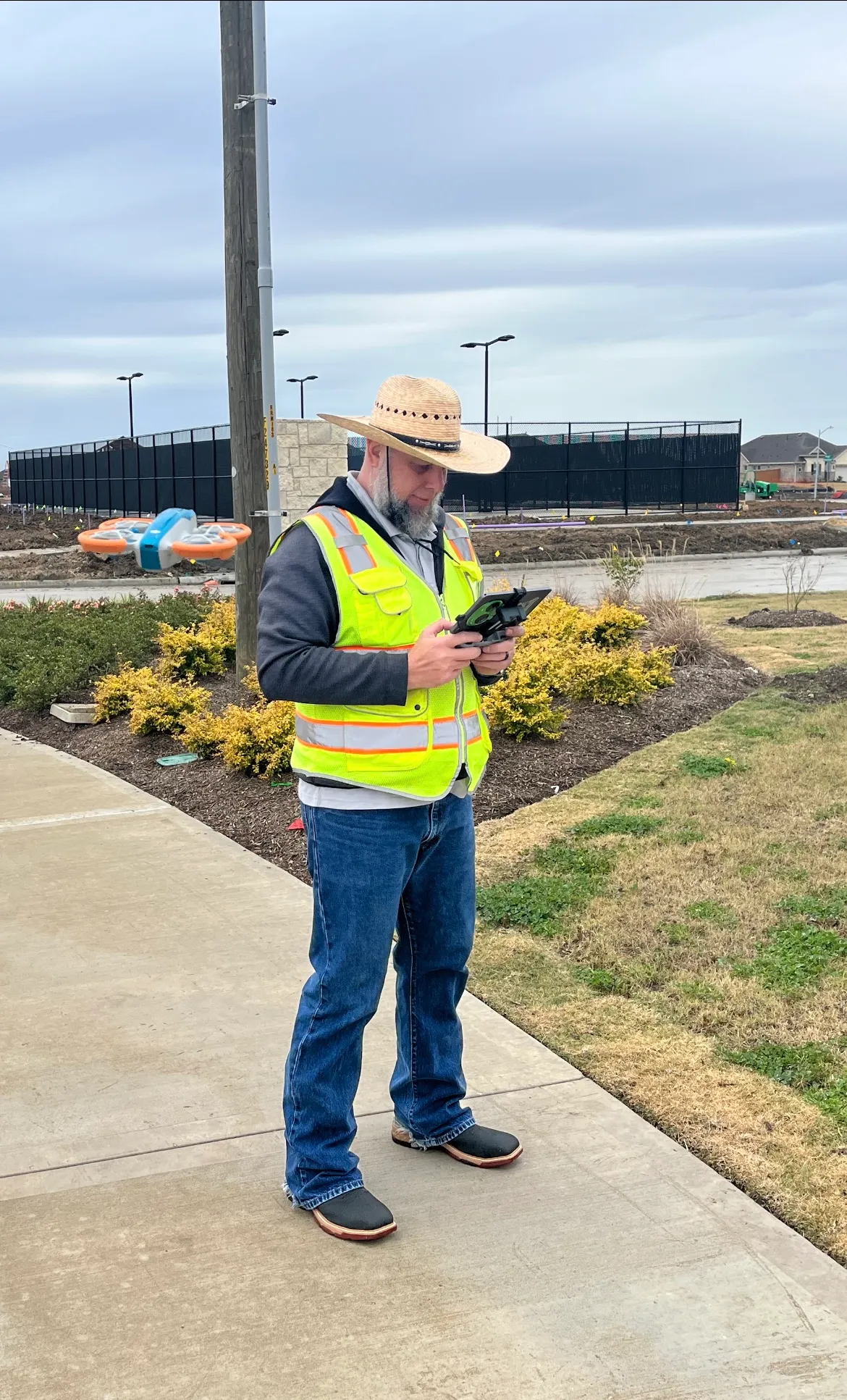 Axis pilot at the controller on a residential development site, the survey drone on the pavement behind them.